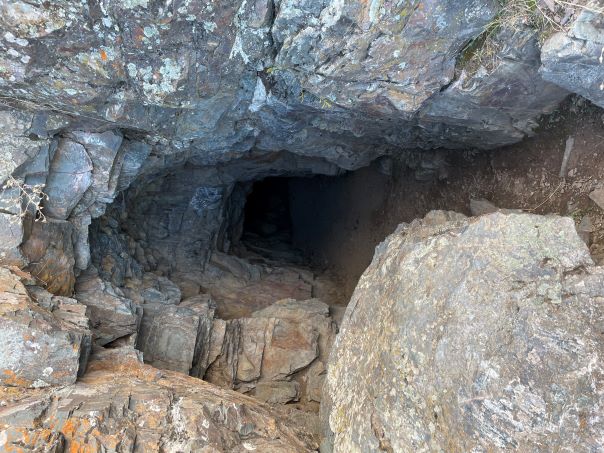 Entrance to a mine; a deep dark hole down in lichen covered rocks. It's about 3 feet wide and 4 feet high. You can see in about 20 feet before it gets too dark.